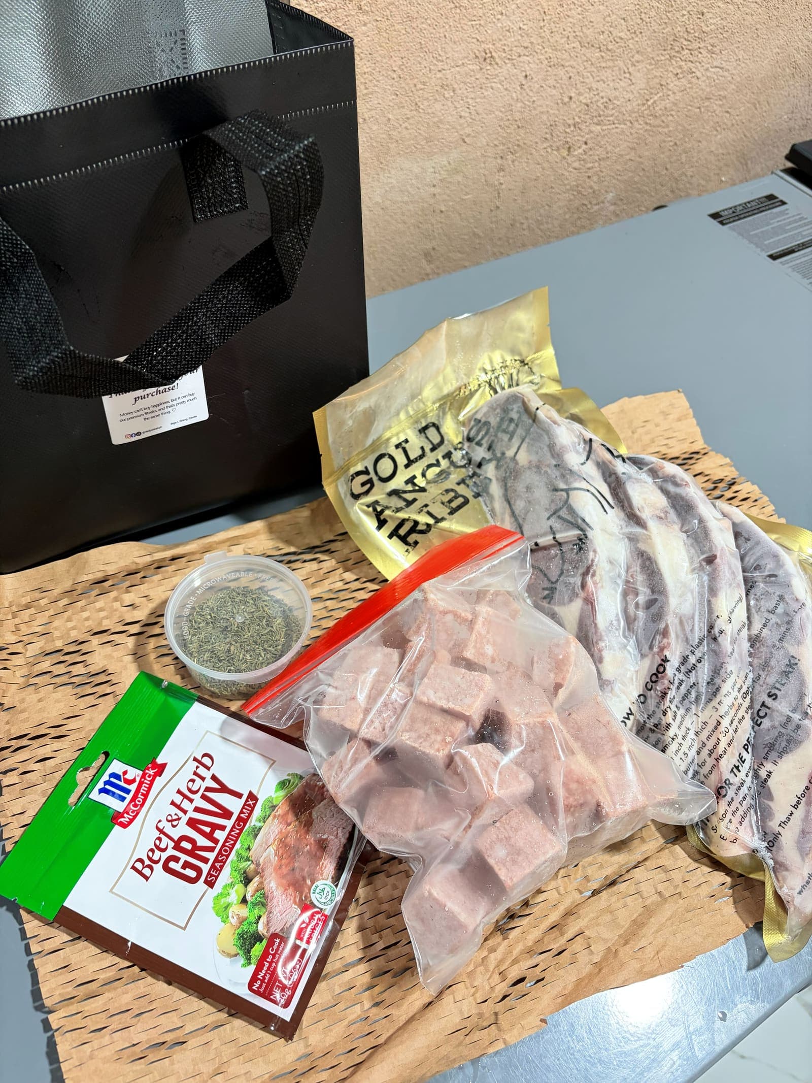 A Gold Artisan ribeye pack and wagyu cubes laid out with thyme and gravy mix beside the insulated bag