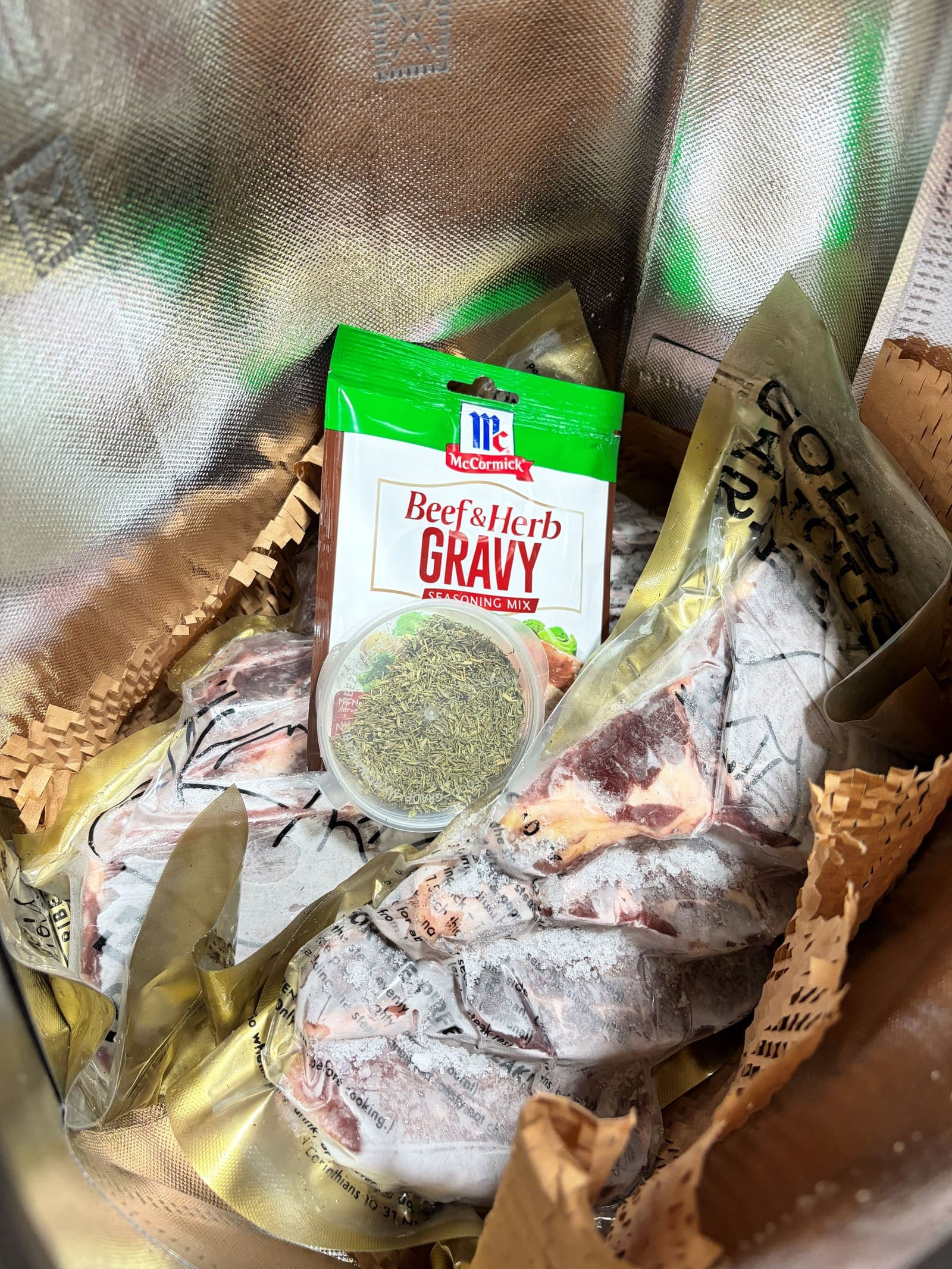 Looking down into a Daily Steak PH insulated bag, vacuum-sealed steaks packed cold with kraft filler and a gravy mix